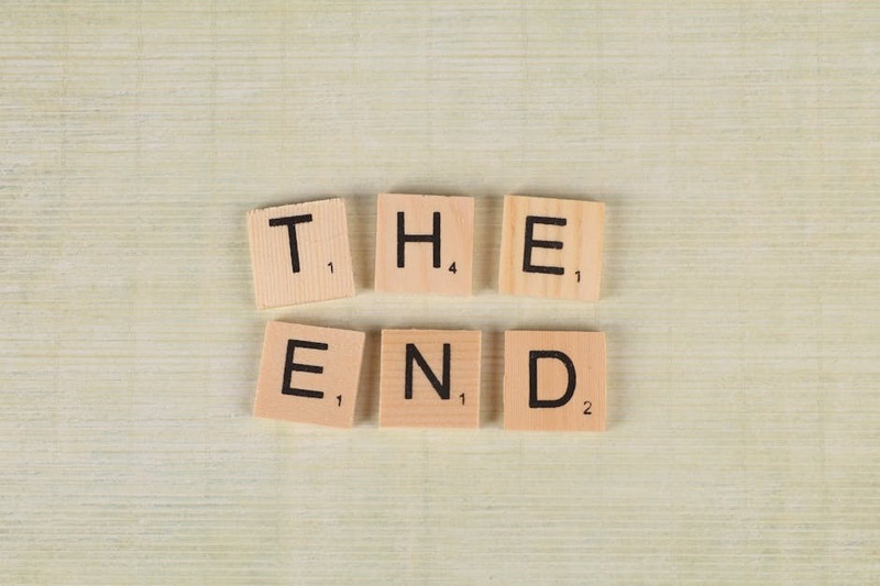 Close-up of Scrabble tiles spelling 'The End' on a simple wooden background for creative concepts.