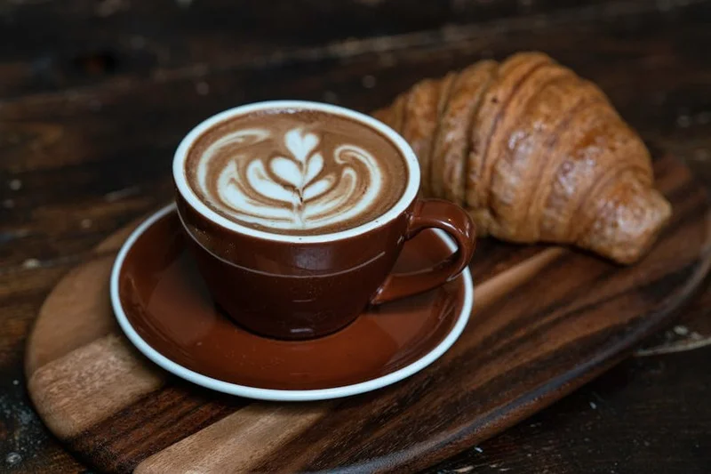 Detalhe de uma arte latte ao lado de um croissant perfeitamente assado