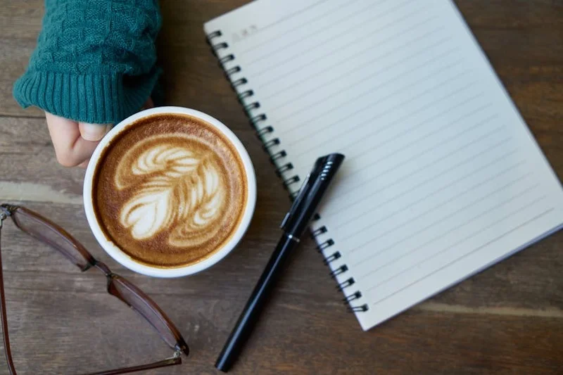 Mãos segurando um caderno e caneta, fazendo anotações sobre harmonização de café e sobremesa