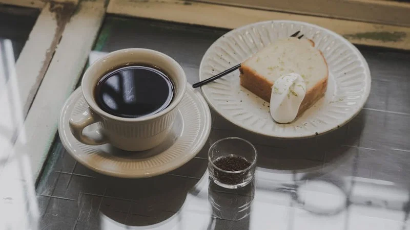Foto aérea de uma xícara de café e uma pequena sobremesa elegantemente arranjadas em uma mesa de madeira